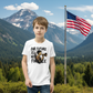 A teen boy stands in a National Park wearing a white tshirt that says "Our Future Is Not For Sale"